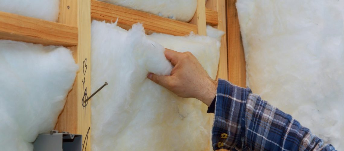 Worker in insulating rock wool insulation in wooden frame for future house walls for comfortable